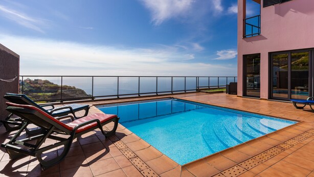 Piscina com espreguiçadeiras em terraço com vista para o oceano.