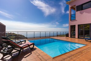 Ein Swimmingpool mit Liegestühlen auf einer Terrasse mit Blick auf den Ozean.