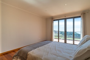 Ein Schlafzimmer mit großem Fenster, einem Bett und Blick auf eine grüne Landschaft.