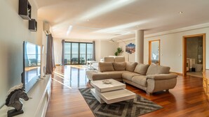 Uma sala de estar moderna com um sofá grande, uma TV de tela plana e um espaço de refeições com uma mesa de centro.