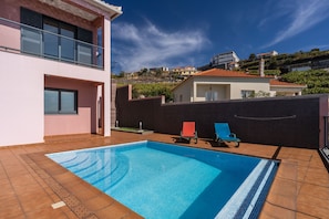 Ein modernes, zweistöckiges Gebäude mit Pool und roten Liegestühlen.