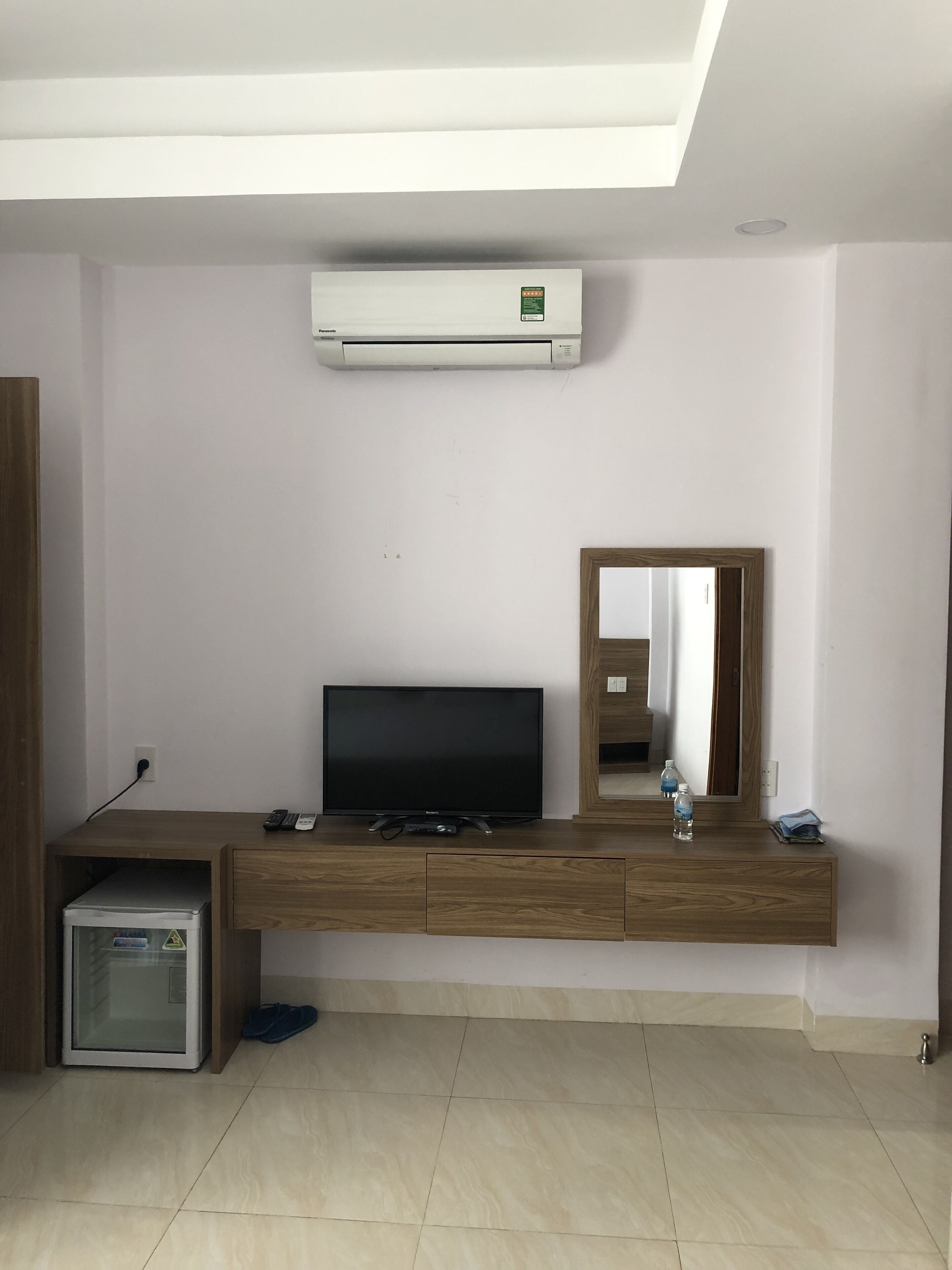 A modern living room with a flat-screen TV, wooden entertainment unit, air conditioning unit, and a mirror.
