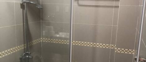 Un box de ducha con paredes de vidrio, un cabezal de ducha de mano y una puerta de vidrio.