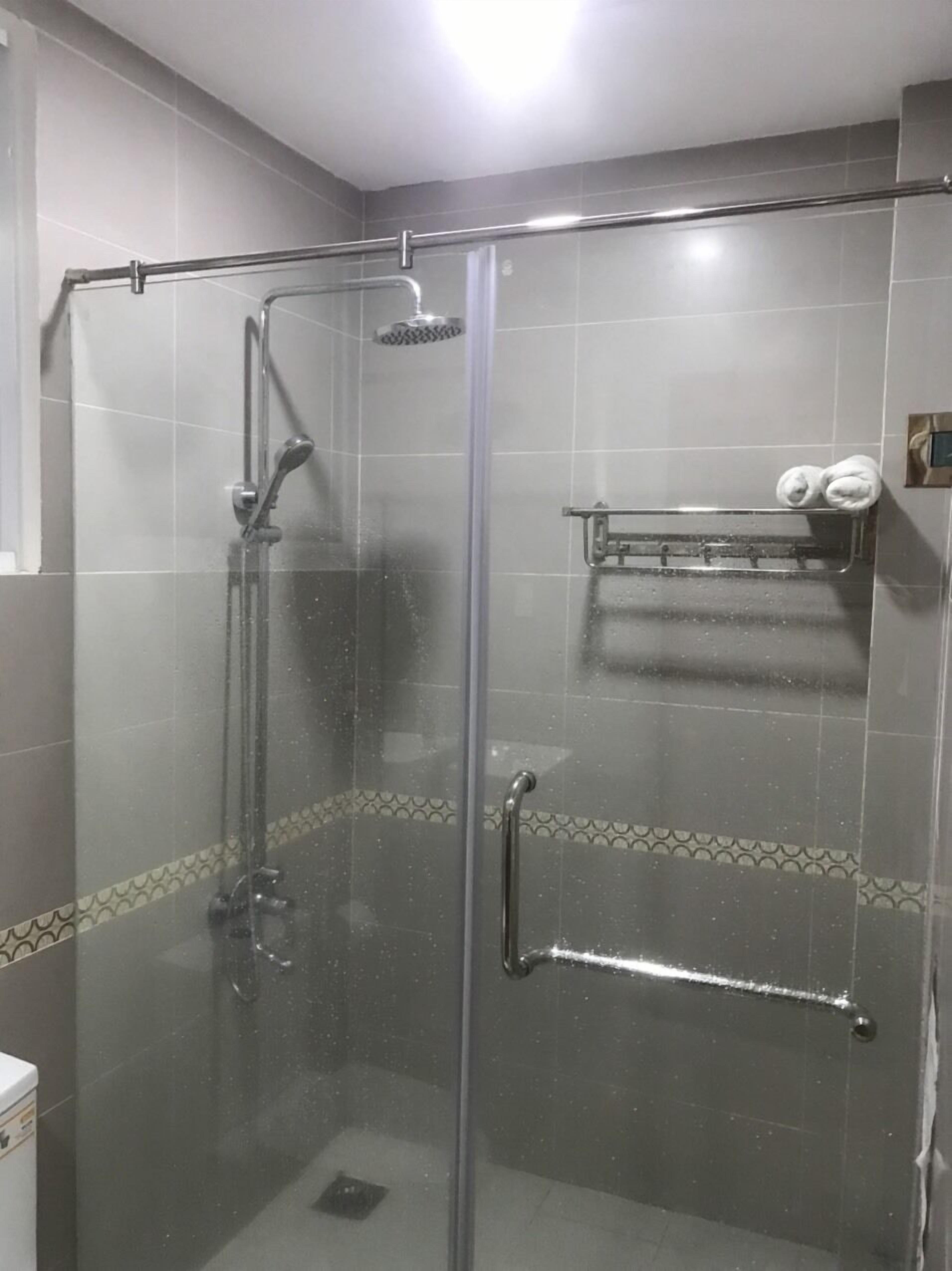A glass-enclosed shower stall with a handheld showerhead, a towel rack with towels, and a small shelf.