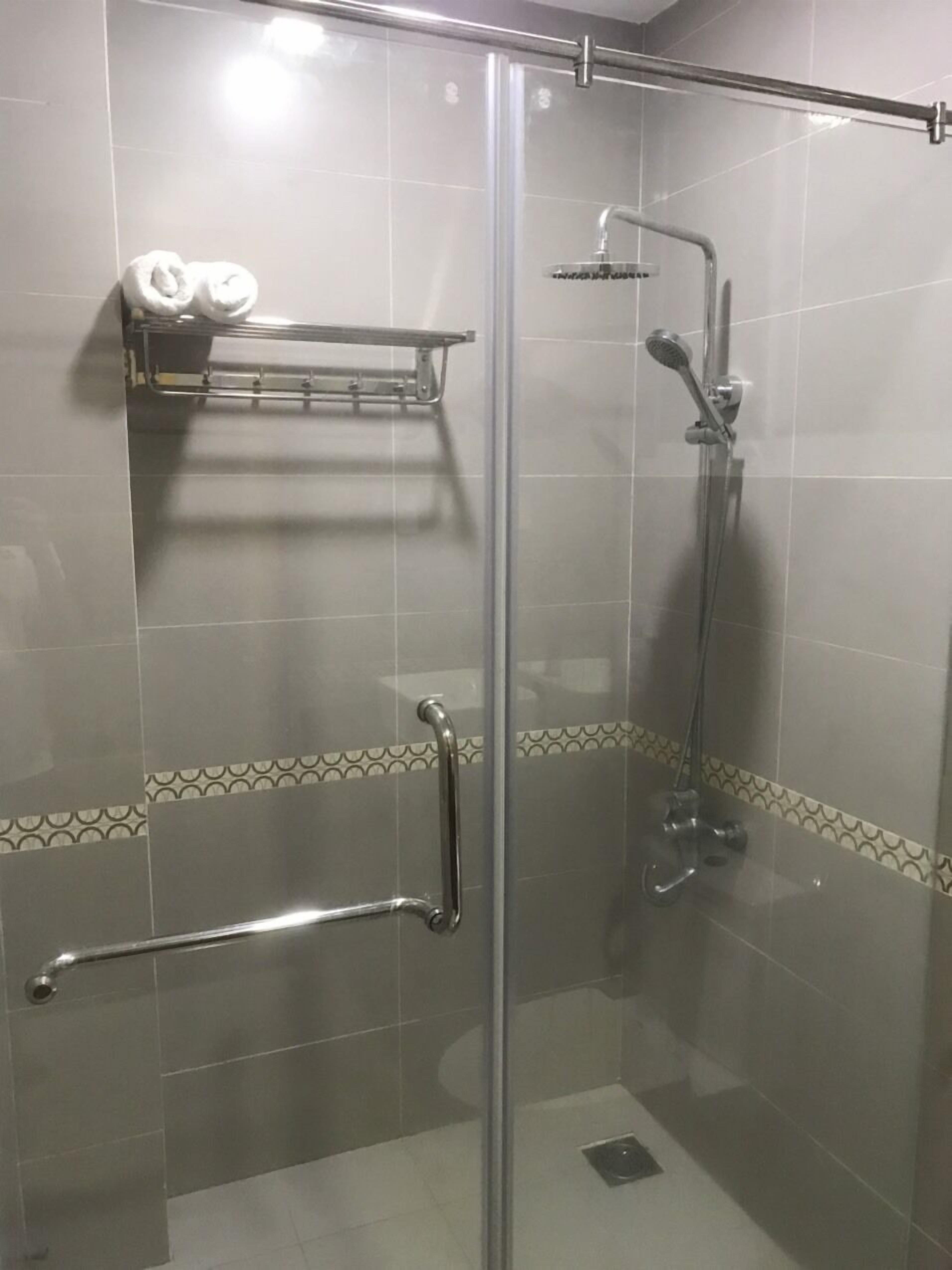 A glass-enclosed shower area with a handheld showerhead, a towel rack with towels, and a grab bar.