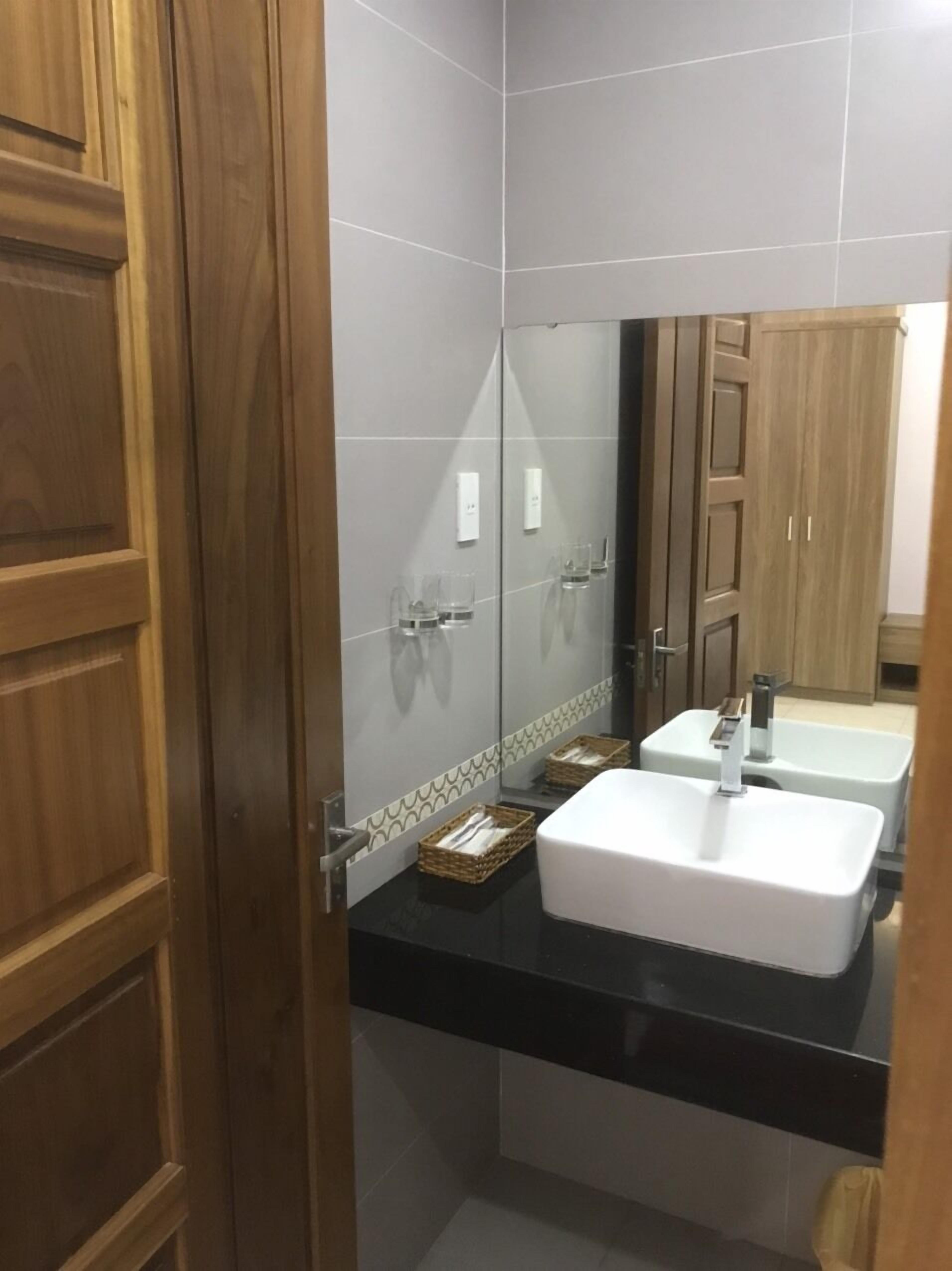 A bathroom with a wooden door, a white sink, a mirror, and a tiled wall.