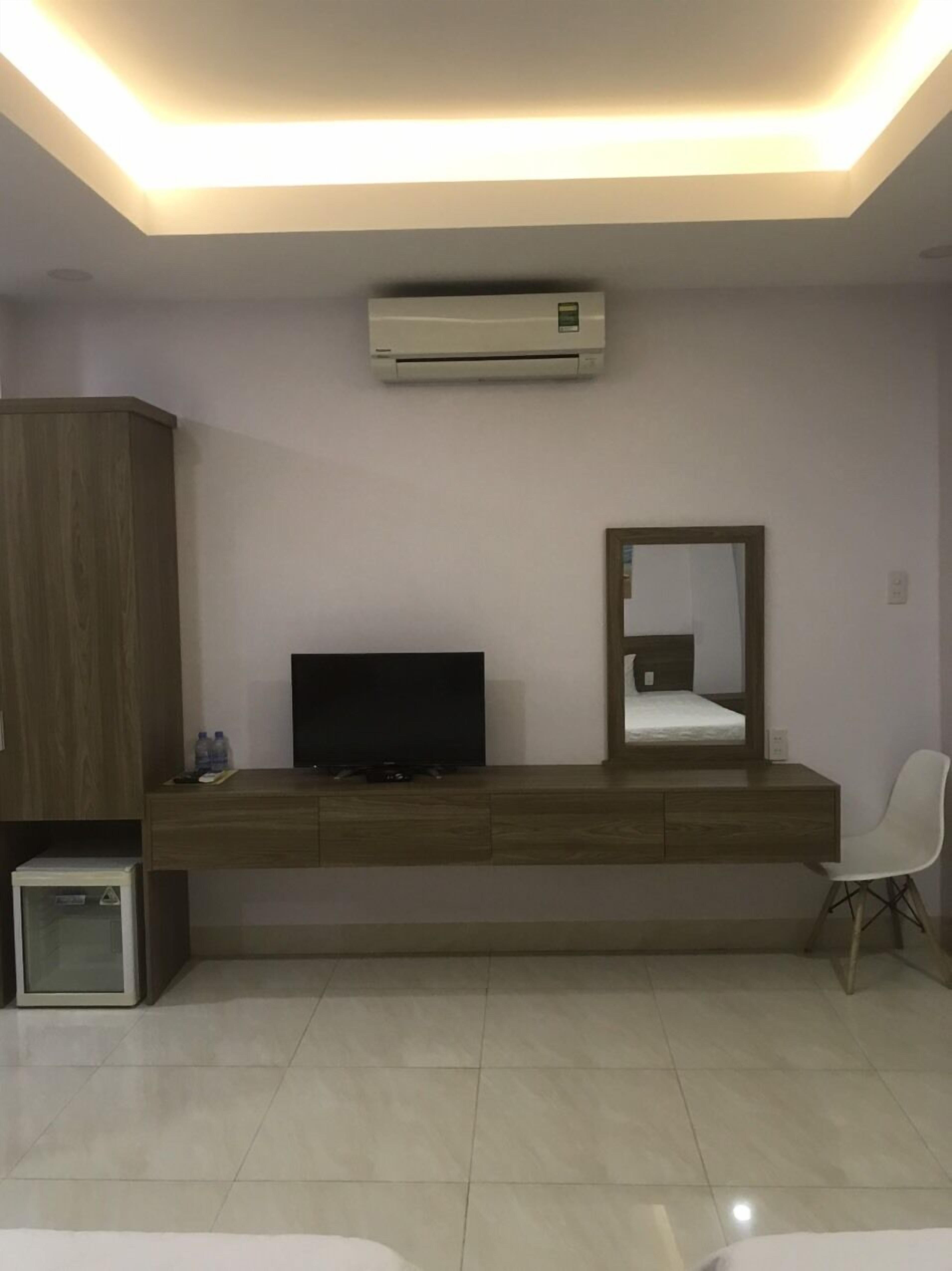 Un dormitorio moderno con televisor empotrado, espejo en la mesita de noche y un pequeño armario.
