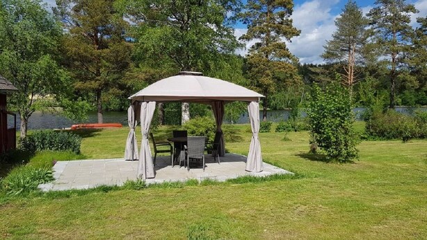 A gazebo with a table and chairs in a grassy area with trees and a lake in the background.