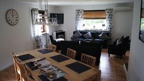 A cozy living room with a wooden dining table, a sofa set, and a clock on the wall.