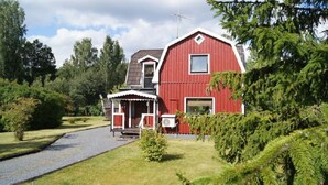 A red barn with a porch, surrounded by greenery and trees.