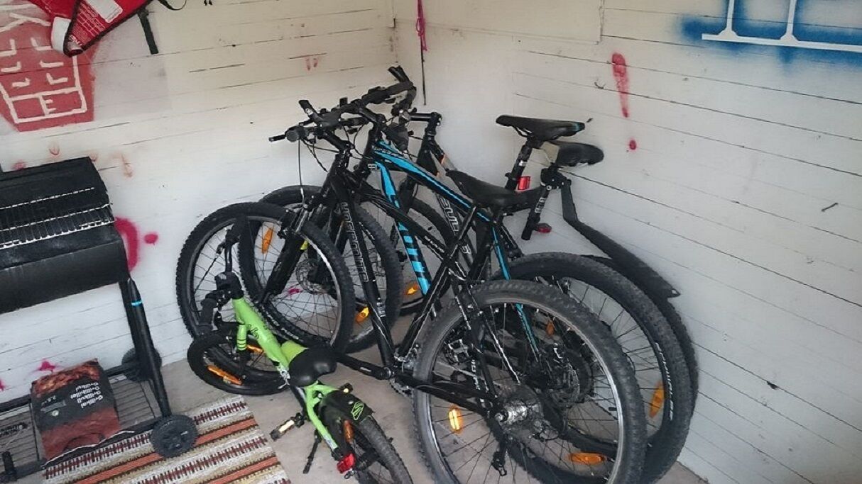 Una habitación con una pared blanca, una estantería negra con objetos, y dos bicicletas apoyadas contra la pared.