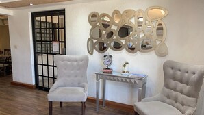 Two upholstered chairs with a tufted design, a small table with decorative items, and a decorative wall piece. - Casagrande Hotel (Monclova)