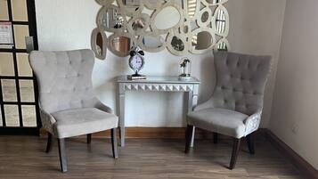 A room with two grey upholstered armchairs, a small white console table with a clock and decorative items, and a wooden herringbone floor.