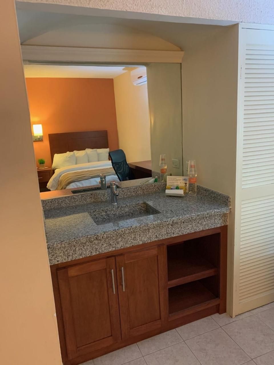 A hotel bathroom with a granite countertop, a sink, a mirror, and wooden cabinets.