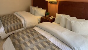 A hotel room with two beds, a nightstand with a phone, and a wall-mounted lamp. - Casagrande Hotel (Monclova)