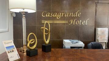 A reception desk with a sign reading "Casagrande Hotel," a lamp, a Canon printer, and a framed brochure.