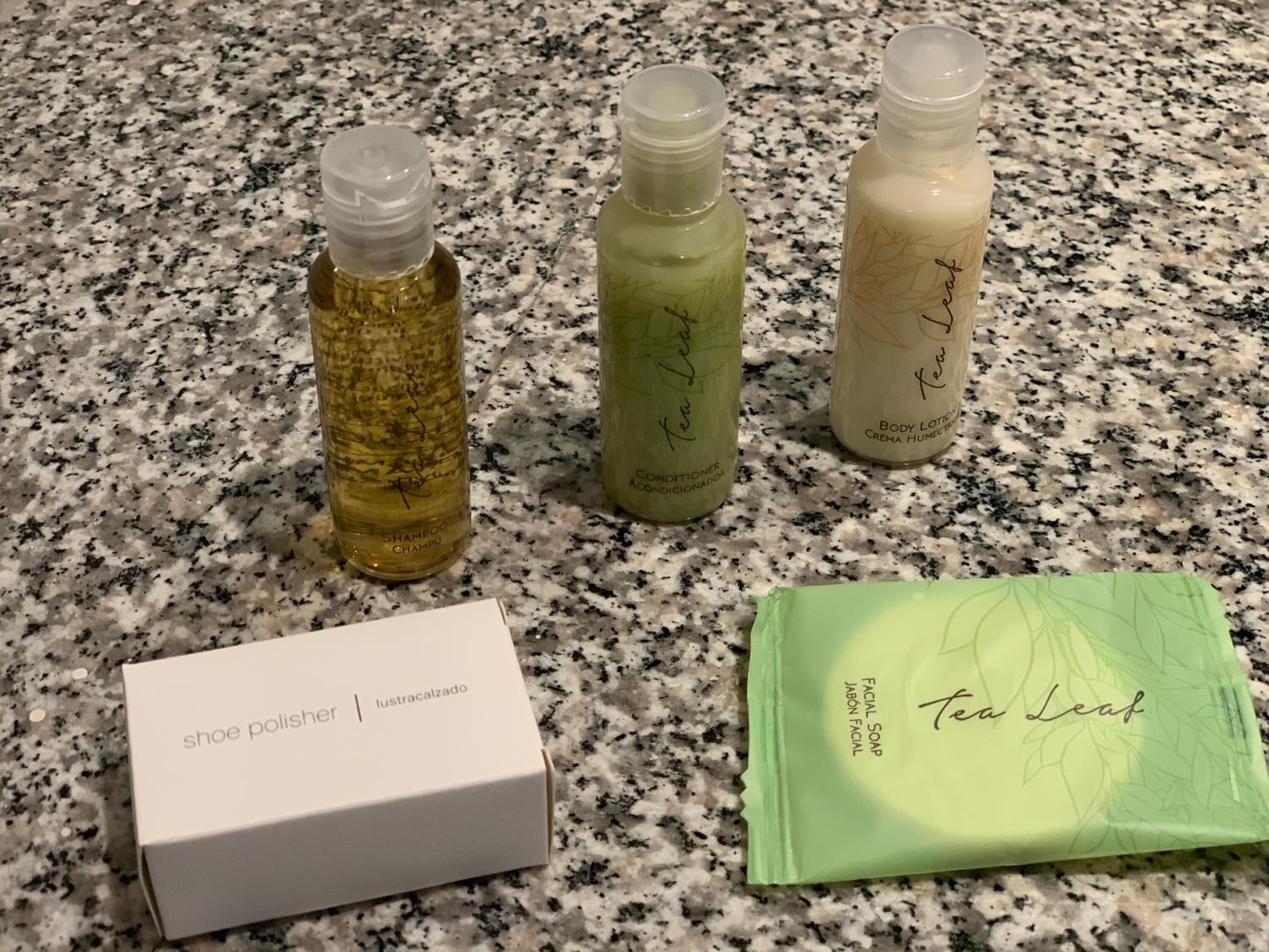 Tres botellas de loción corporal con extracto de té, una caja de limpiador de zapatos y un paquete verde de jabón facial sobre una encimera de granito.