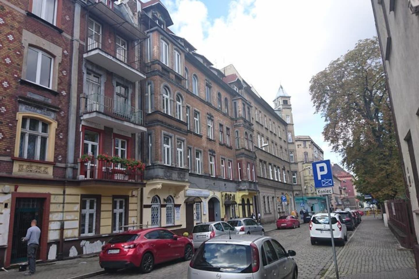 Een straat met meerverdiepingen tellende gebouwen, geparkeerde auto's en een zichtbaar parkeersbord.