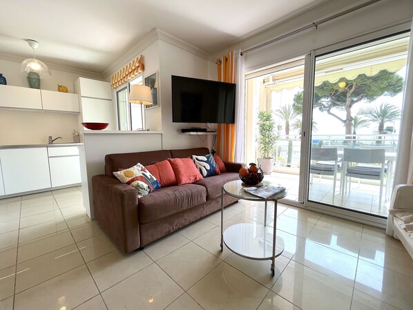 A modern living room with a brown sofa, a glass coffee table, and a flat-screen TV mounted on the wall. - L'appartement Royal Palm (Cannes)