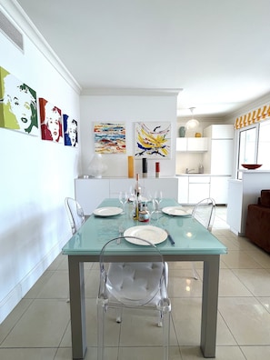 A modern dining area with a glass table, clear chairs, and a white cabinet in the background. - L'appartement Royal Palm (Cannes)