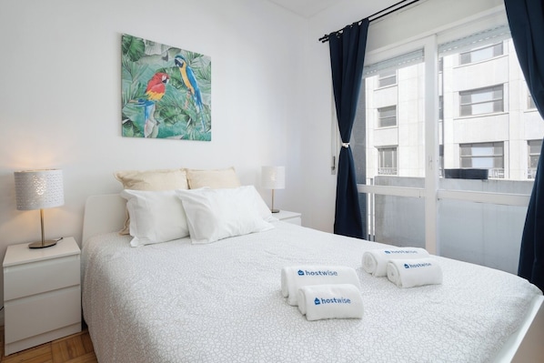 Relax in a stylish room with a large bed, colorful artwork, and a window offering a view of the building outside.