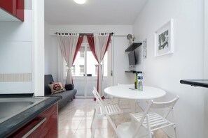 Cozy living space with a kitchenette, dining area, and sofa, featuring a mounted TV and decorative shelf.