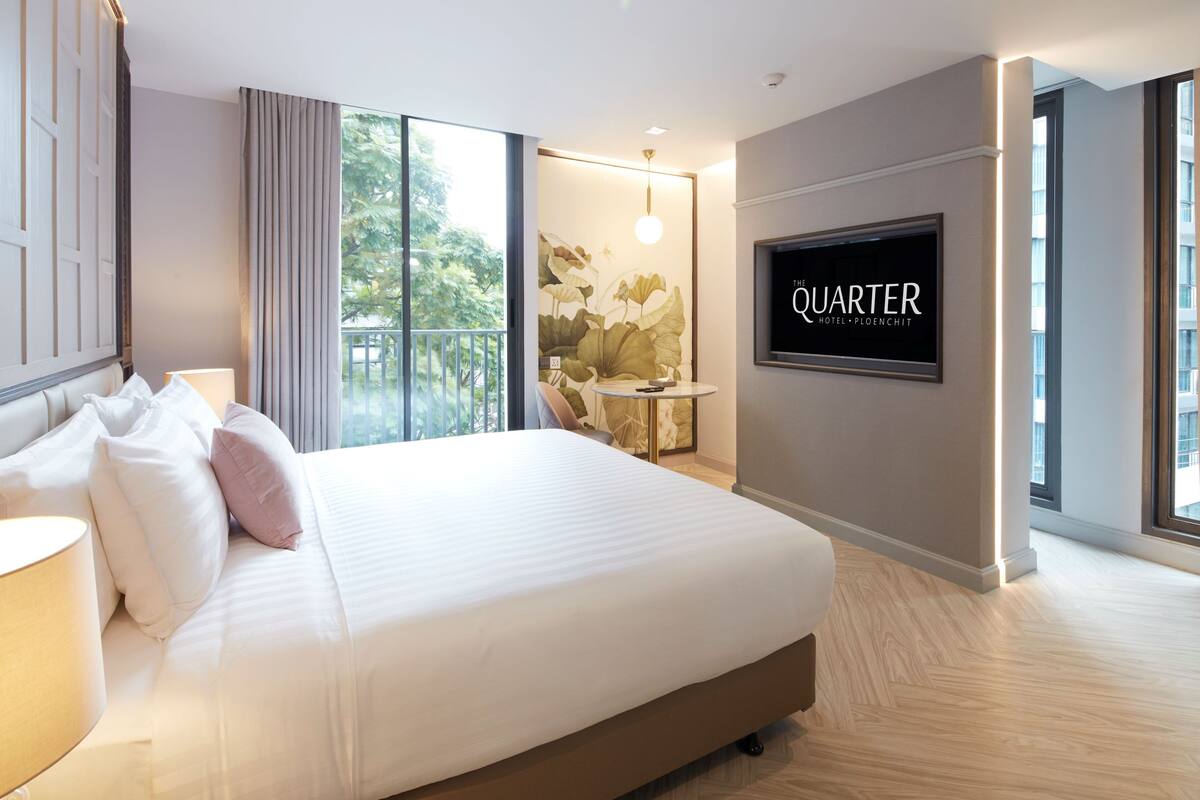 A modern hotel room with a large bed, a TV on the wall, and a balcony with a view of trees.