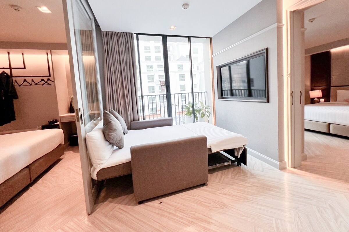 A modern hotel room with a bed, a seating area, a large window, and a view of the city.