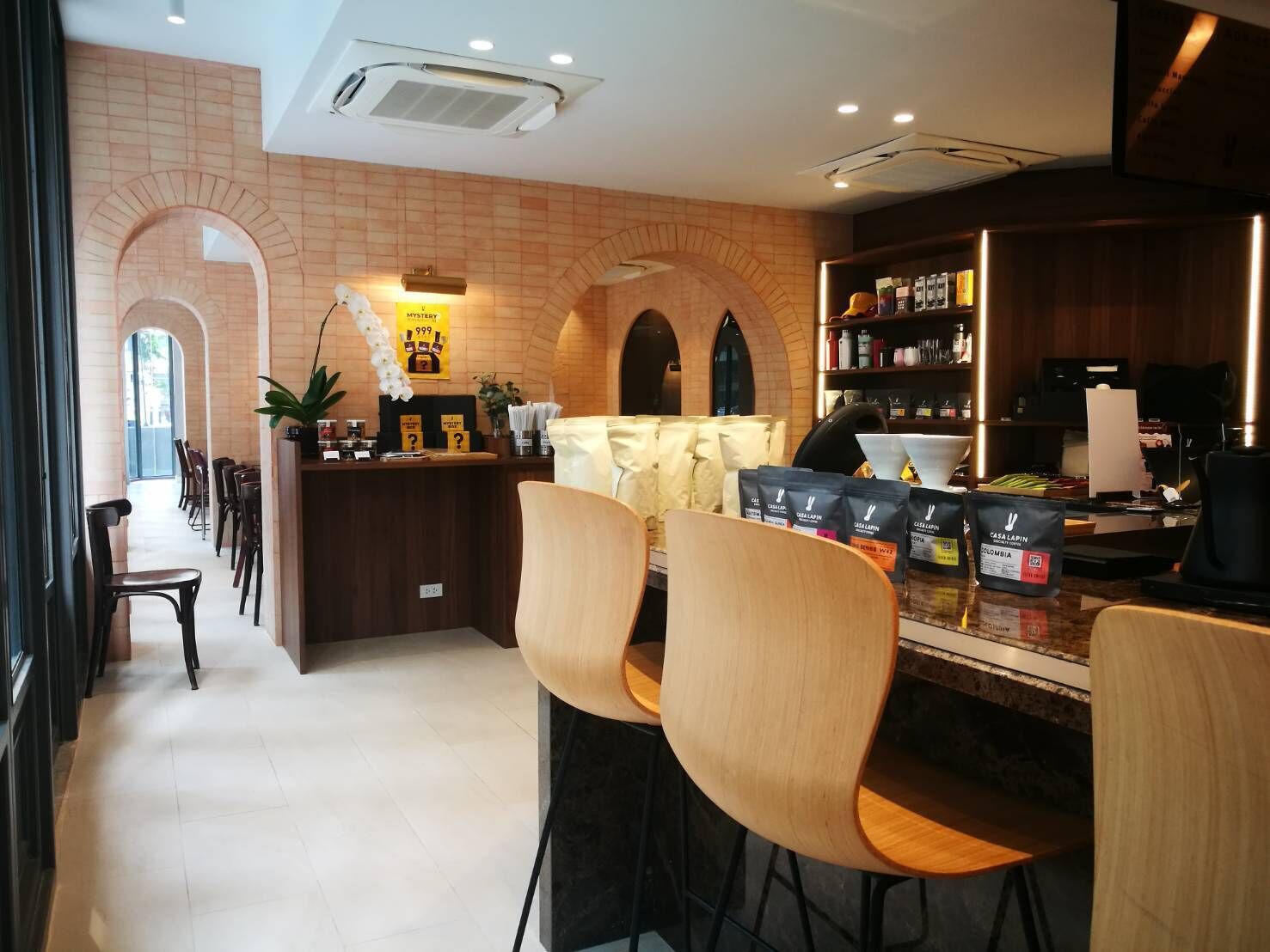 A modern cafe with wooden chairs and tables, a counter with a menu, and a brick wall with arches.