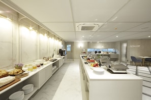 Une cuisine moderne d’hôtel, dotée d’un long comptoir, de divers produits alimentaires et d’un coin salon avec une chaise bleue.