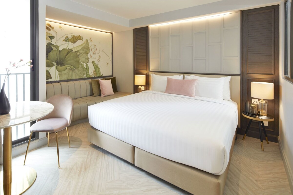 Une chambre d’hôtel moderne dotée d’un grand lit, d’un coin salon avec un canapé et des fauteuils, d’une petite table ronde et d’une œuvre d’art accrochée au mur.