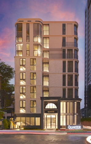 Un hôtel à plusieurs étages au design moderne, avec une entrée imposante portant l’inscription « The Quarter Hotel ».