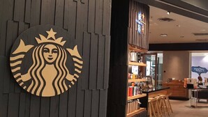 Ein Starbucks-Logo an einer Wand, ein Barbereich mit Barhocker und eine Theke mit verschiedenen Artikeln.