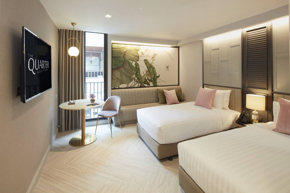 A hotel room with two beds, a TV, a desk with a chair, and a large window with curtains.