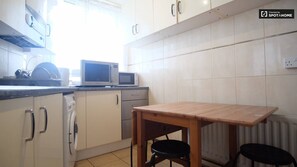Compact kitchen area with a table and stools, featuring white cabinets, a microwave, and a dish rack.