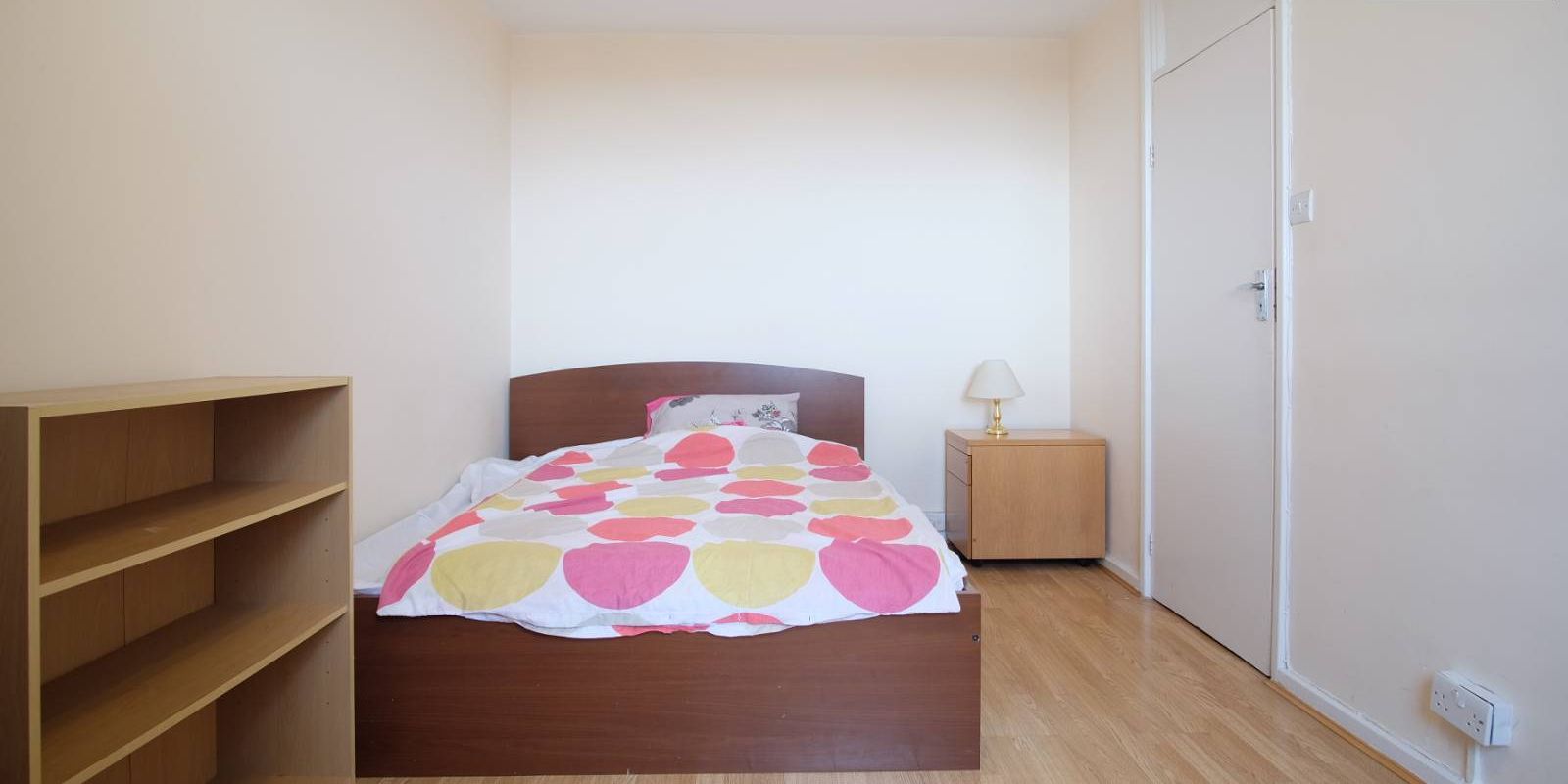 A bedroom with a wooden bed, a bedside table with a lamp, and a wardrobe.