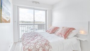 A bedroom with a bed, a nightstand, a wall-mounted shelf, and a large window with a view of the sea. - LE MATELOT 3* - Superbe appartement vue mer - Erquy (Erquy)