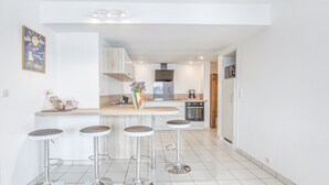 A modern kitchen with a central island, bar stools, and a refrigerator. - LE MATELOT 3* - Superbe appartement vue mer - Erquy (Erquy)