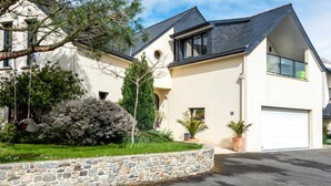 A modern two-story house with a stone retaining wall, a garage, and a well-maintained garden with various plants and a swing set. - L'Abri du Bon Vent - Proche plage - Cancale (Cancale)
