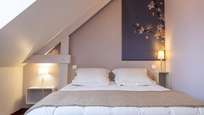 A bedroom with a sloped ceiling, a bed with white linens, two bedside tables with lamps, and a wall-mounted floral decoration. - L'Abri du Bon Vent - Proche plage - Cancale (Cancale)