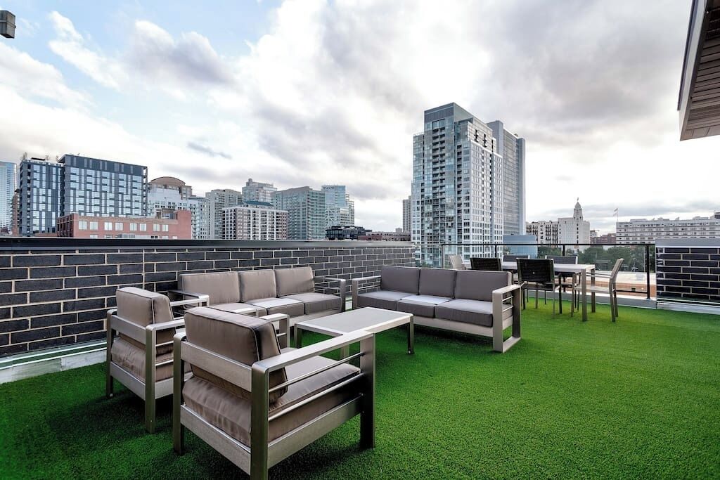 Eine Dachterrasse mit Gartenmöbeln und Blick auf die Skyline der Stadt, begleitet von einer Backsteinmauer.