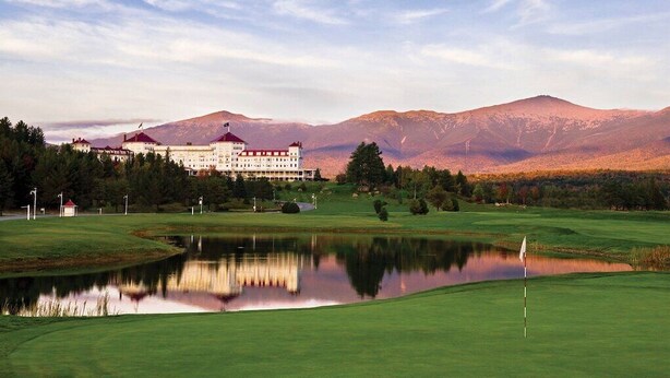 A golf course with a pond, a large building with a red roof, and mountains in the background. - Ski-in/Out 1st on Mountain Lux Suite + Kitchenette (Bretton Woods)