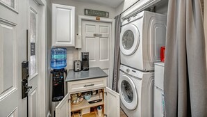 A compact laundry room with a water dispenser, coffee maker, and stacked washing machines. - Ski-in/Out 1st on Mountain Lux Suite + Kitchenette (Bretton Woods)