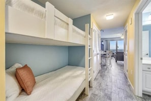Una habitación con literas, una mesita y vistas por una puerta abierta.