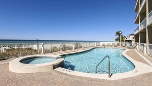 A swimming pool with a hot tub, surrounded by a white fence, overlooking a beach.