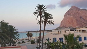 Un hôtel en bord de mer, agrémenté de palmiers, offrant une vue sur l’océan et avec une montagne imposante en arrière-plan.