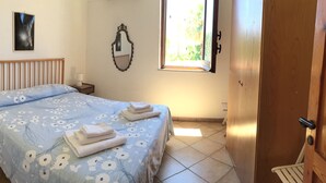Une chambre à coucher comprenant un lit, une table de chevet, une lampe de chevet, un miroir et une fenêtre.