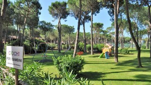 Un espace de jeux avec des balançoires et des toboggans, entouré d’arbres et de verdure.