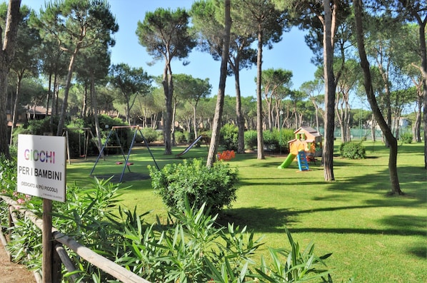 A park with playground equipment, including swings and slides, surrounded by trees and greenery.