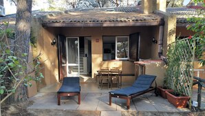Un petit espace extérieur comprenant deux chaises longues, une table et des chaises, le tout entouré d’un petit muret et agrémenté de plantes en pot.